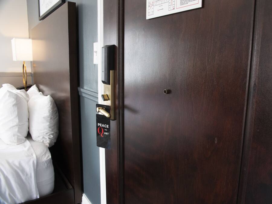 A hotel room with a bed, a nightstand, a lamp, and a door with a 'Peace Quiet' sign.