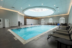 A large indoor swimming pool with a skylight, lounge chairs, and a tiled floor.