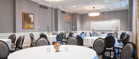 A conference room with round tables, chairs, a whiteboard, and a chandelier.