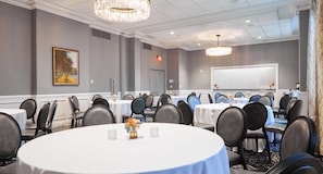 A conference room with round tables, chairs, a whiteboard, and a chandelier. - The Queensbury Hotel (Glens Falls)