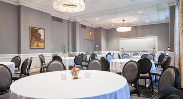A conference room with round tables, chairs, a whiteboard, and a chandelier.