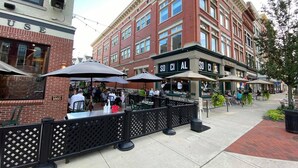 A brick building with outdoor seating and umbrellas, a sign reading "SO CAL," and a fenced area with tables and chairs. - The Queensbury Hotel (Glens Falls)