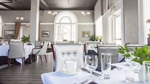 A restaurant with high ceilings, arched windows, and modern lighting. Tables are set with white tablecloths and silverware. - The Queensbury Hotel (Glens Falls)