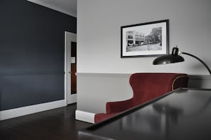Une pièce avec un plancher en bois foncé, une chaise rouge, un bureau noir et une photographie en noir et blanc encadrée accrochée au mur.