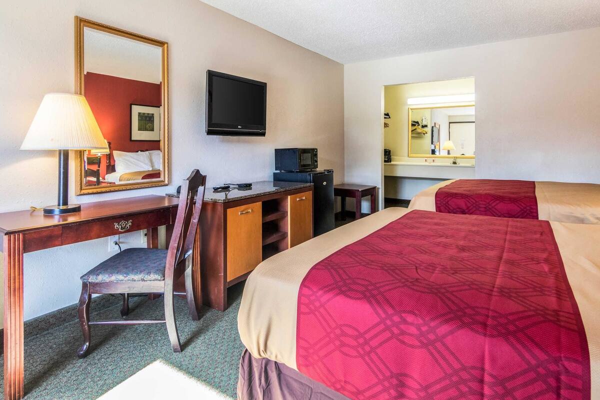 Ein Hotelzimmer mit einem Bett, einem Schreibtisch mit Stuhl, einem Fernseher, einer Mikrowelle und einem Spiegel.