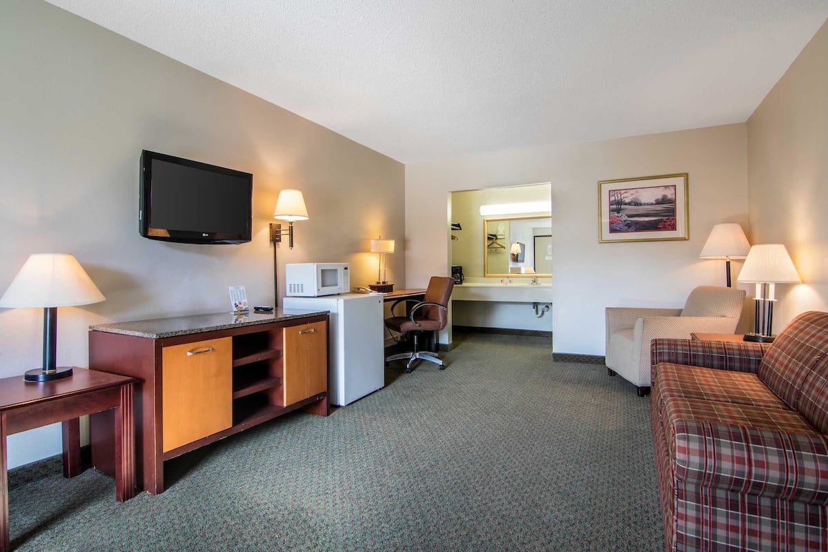 Ein Hotelzimmer mit Schreibtisch, Fernseher, Mikrowelle, Sessel, Schlafsofa und Bett.