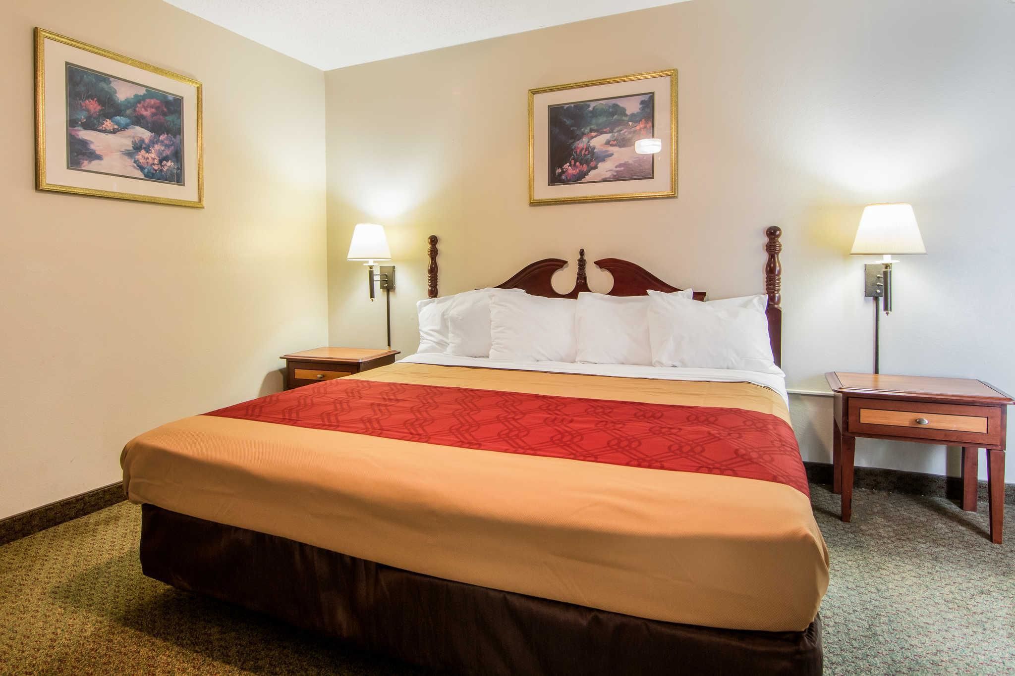 A hotel room with a large bed, two bedside tables, two wall-mounted lamps, and two framed pictures on the walls.