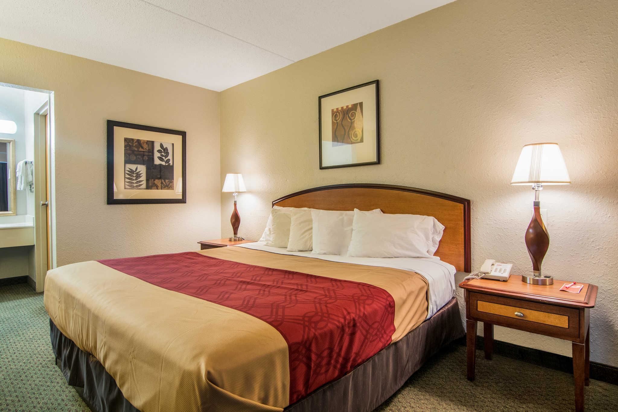A hotel room with a large bed, two bedside tables, a nightstand, and two wall-mounted lamps.