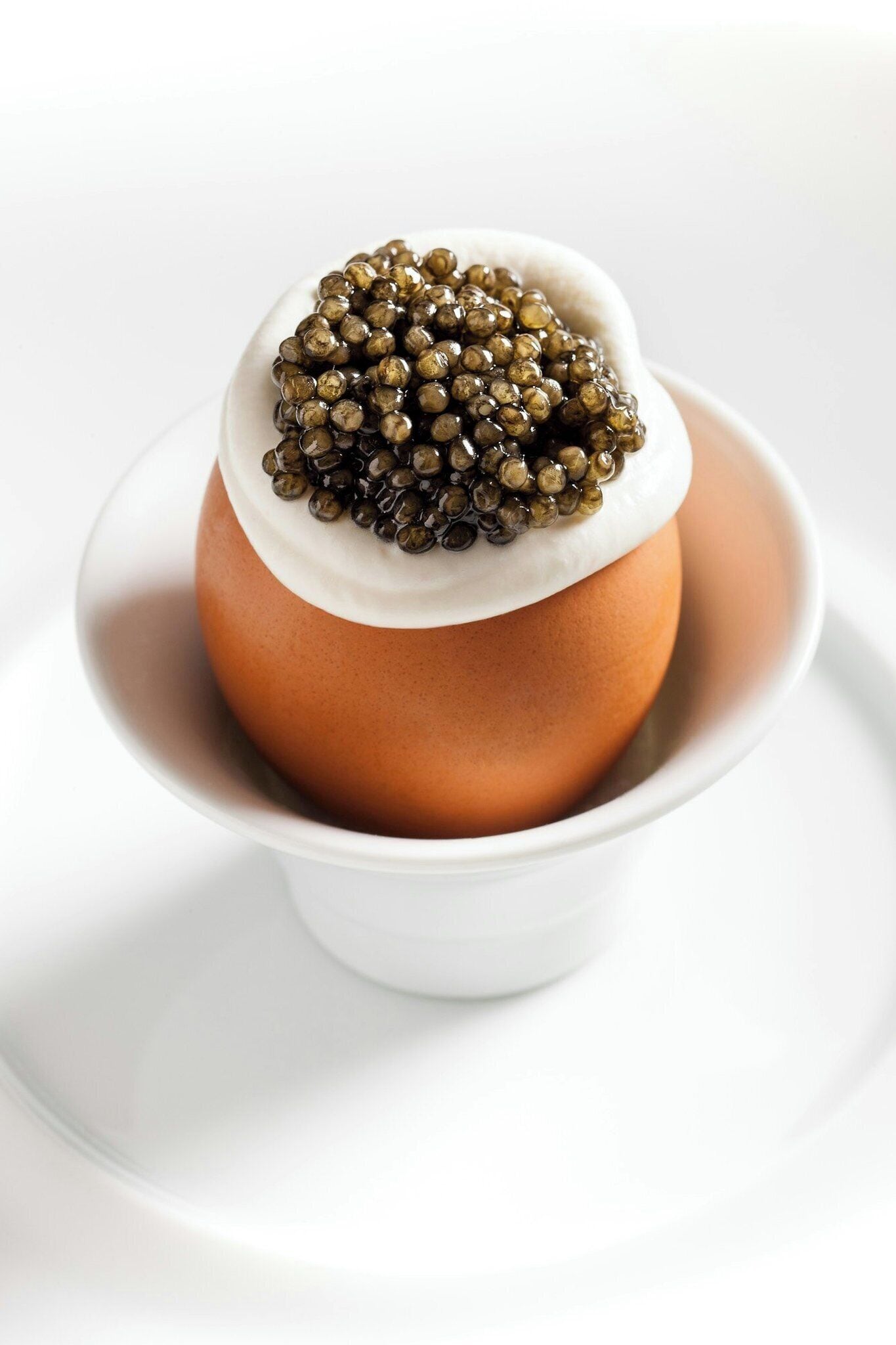 A white ceramic cup with a brown object inside, possibly a dessert, on a white plate.