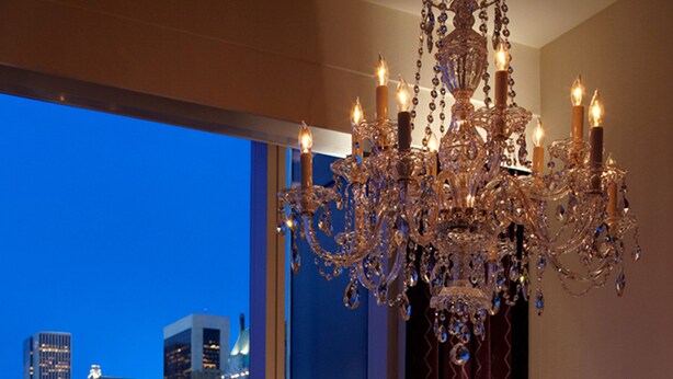 Une salle à manger avec une table dressée pour quatre personnes, un lustre et une vue sur la ville à travers de grandes fenêtres.