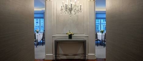A hallway with a central console table, a chandelier, and two tables set for dining with chairs.