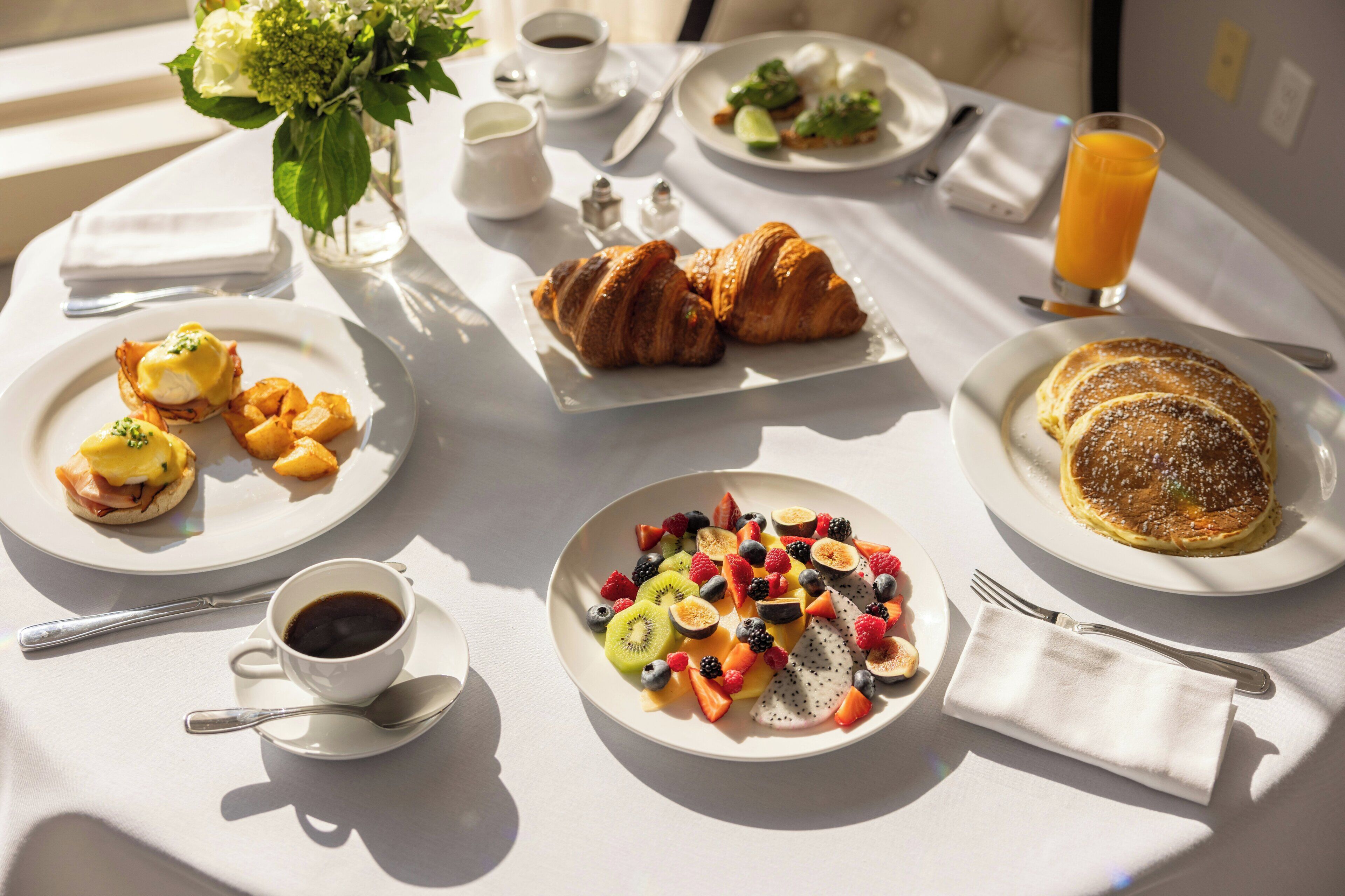 A breakfast table with various dishes including eggs, croissants, and fruit.