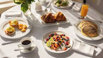 A breakfast table with various dishes including eggs, croissants, and fruit.