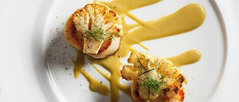 A white plate with two scallops and a yellow sauce.