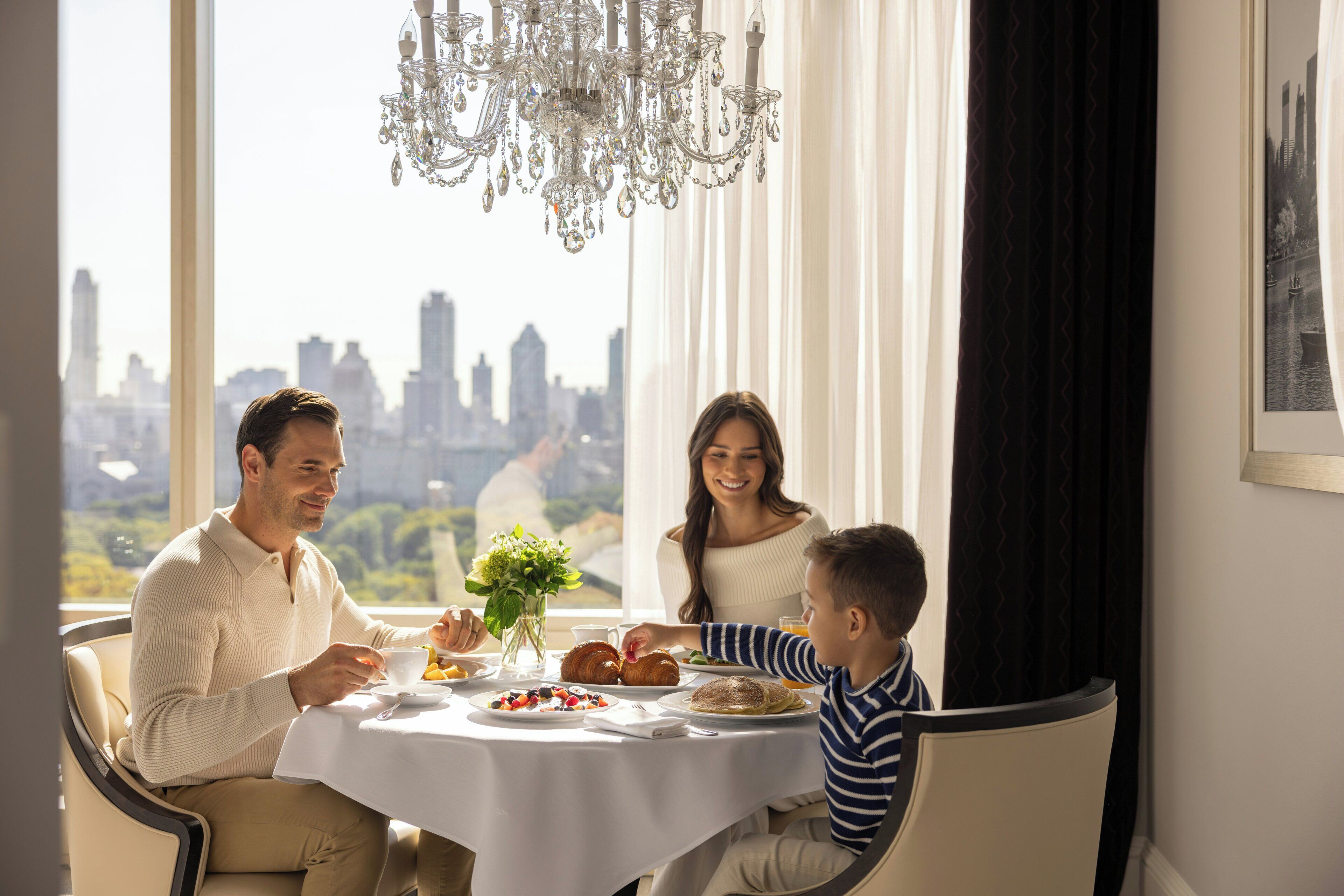 A family dining at a table with a city view, a chandelier, and a framed picture on the wall.