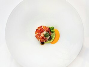 Een wit bord met een zeevruchtengerecht, groene groenten en een gele saus.