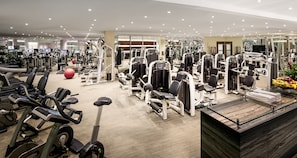 Un gimnasio moderno con diversos equipos de cardio y entrenamiento de fuerza, una recepción y una pared de espejos.