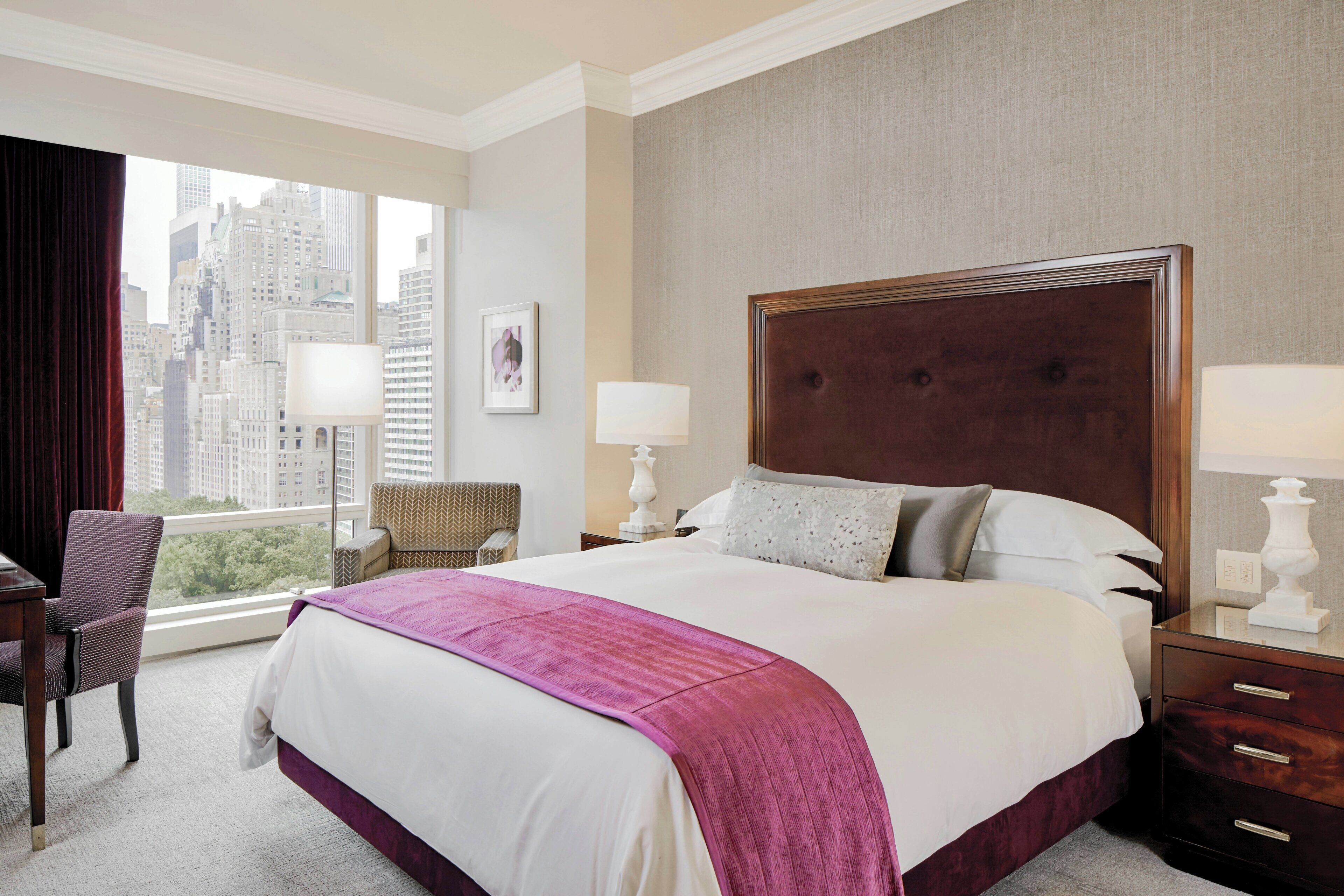 A hotel room with a large bed, two bedside tables with lamps, a chair, a view of the cityscape through the window, and a cityscape view from the window.