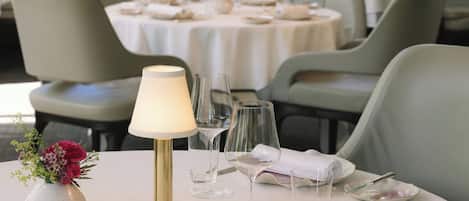 Una mesa de comedor dispuesta con mantel blanco, cristalería y un florero con flores.