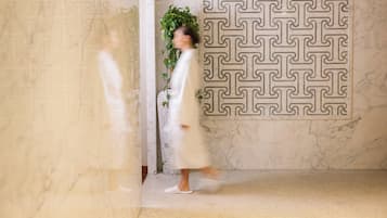 A room with a patterned wall, a potted plant, and a person walking.