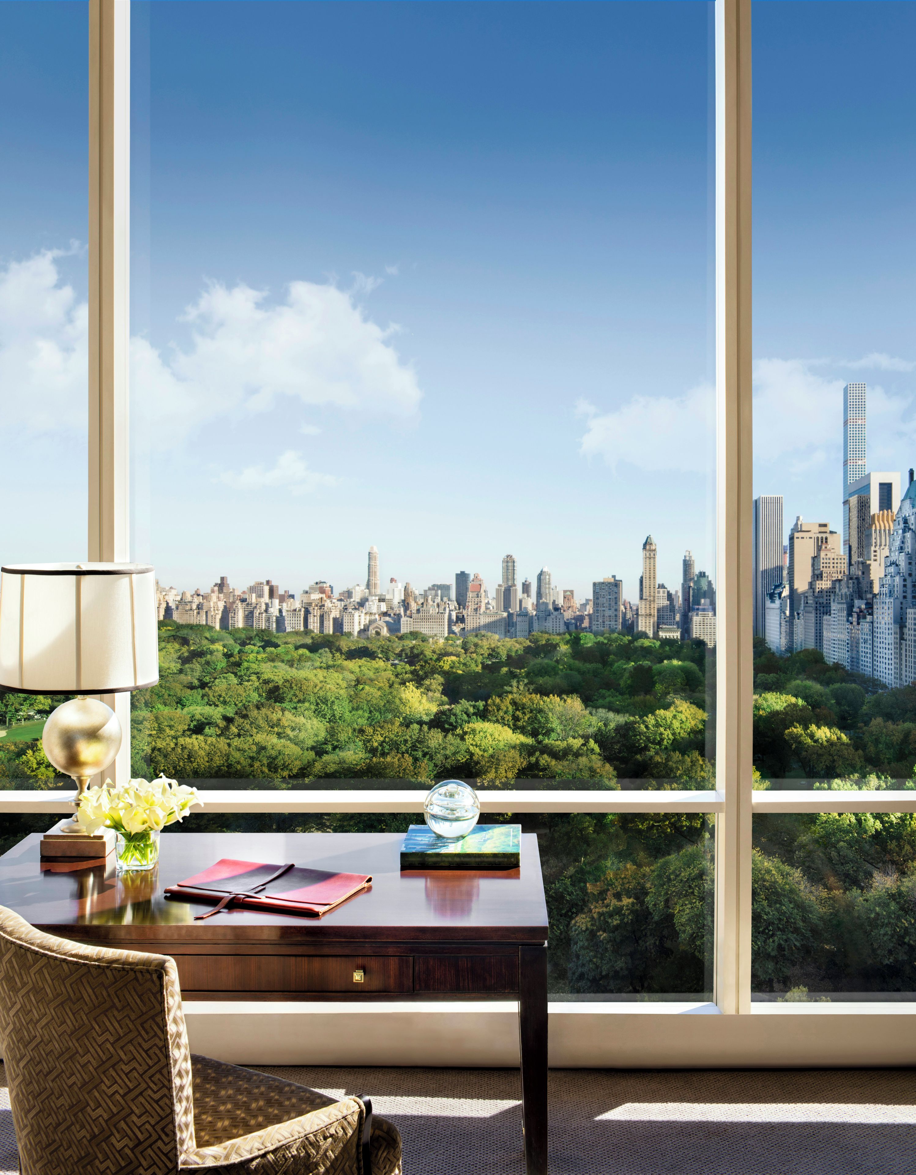 A room with a desk, chair, and a large window offering a city skyline view.