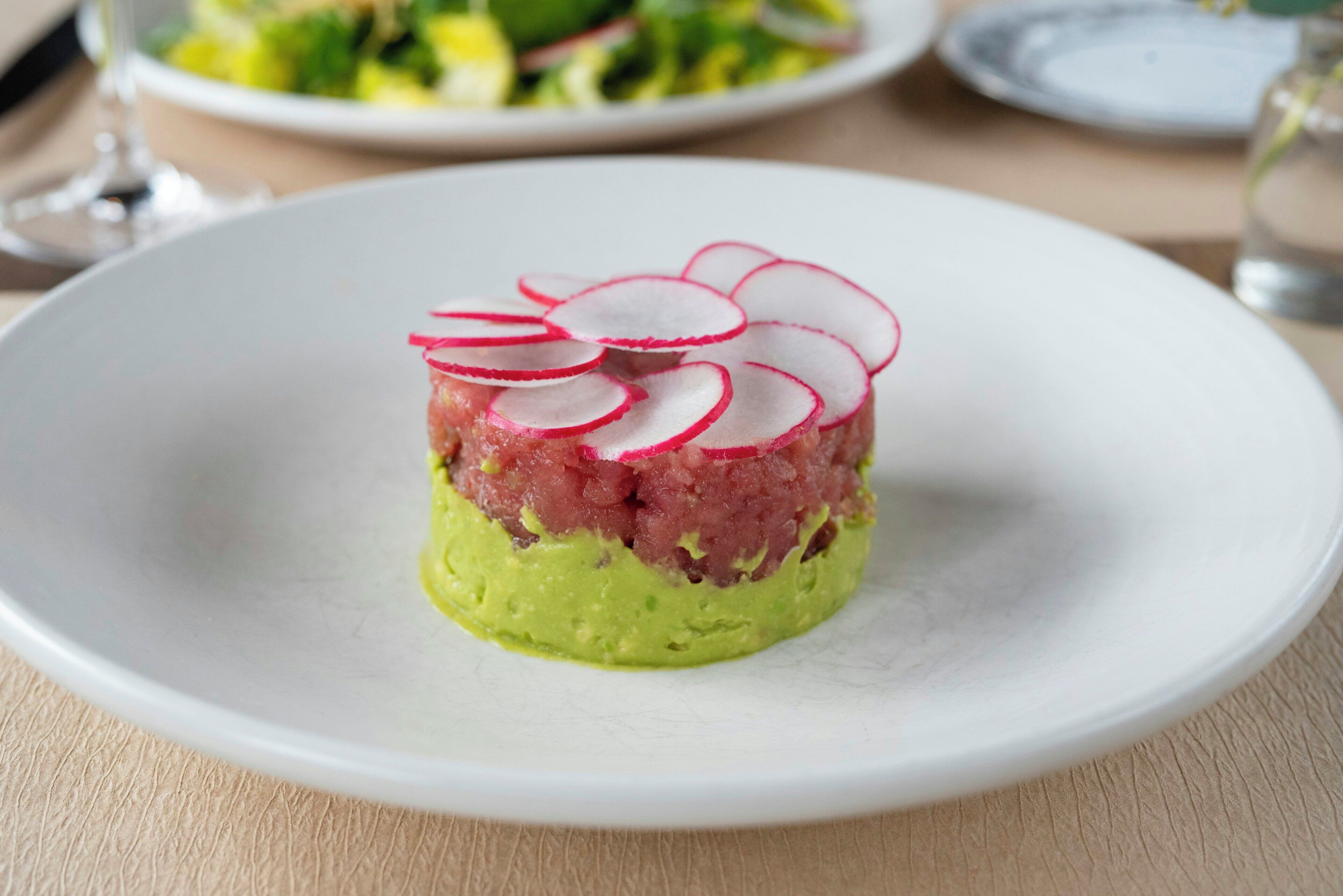 Un plato con un guiso en capas, posiblemente un tartare, sobre un plato blanco.