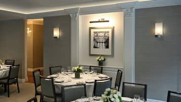 A dining area with a round table set for six, surrounded by chairs, with a framed picture above the table and wall-mounted lighting on either side.