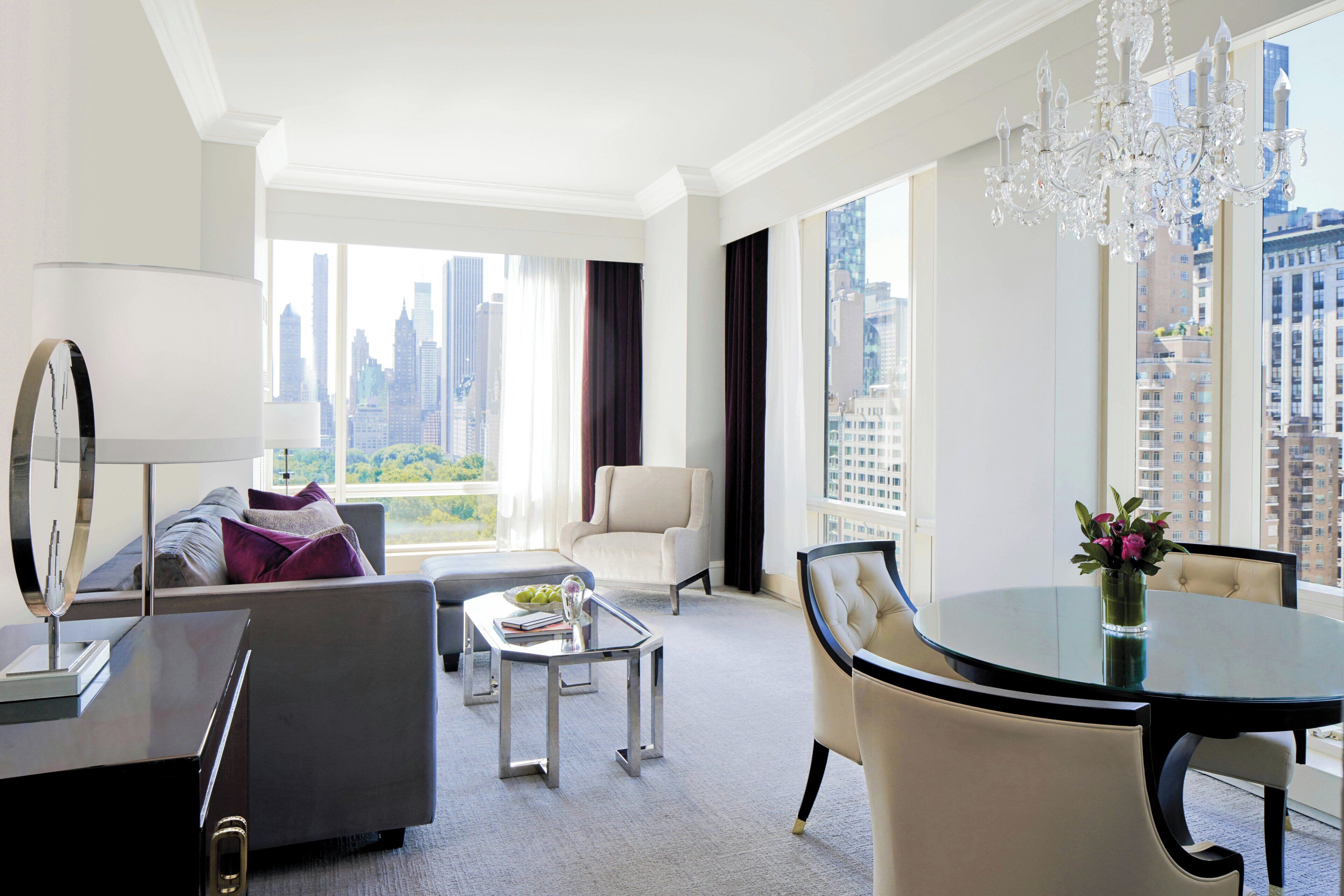 Una habitación de hotel moderna con vista a la ciudad, un área de comedor y una lámpara de araña grande.