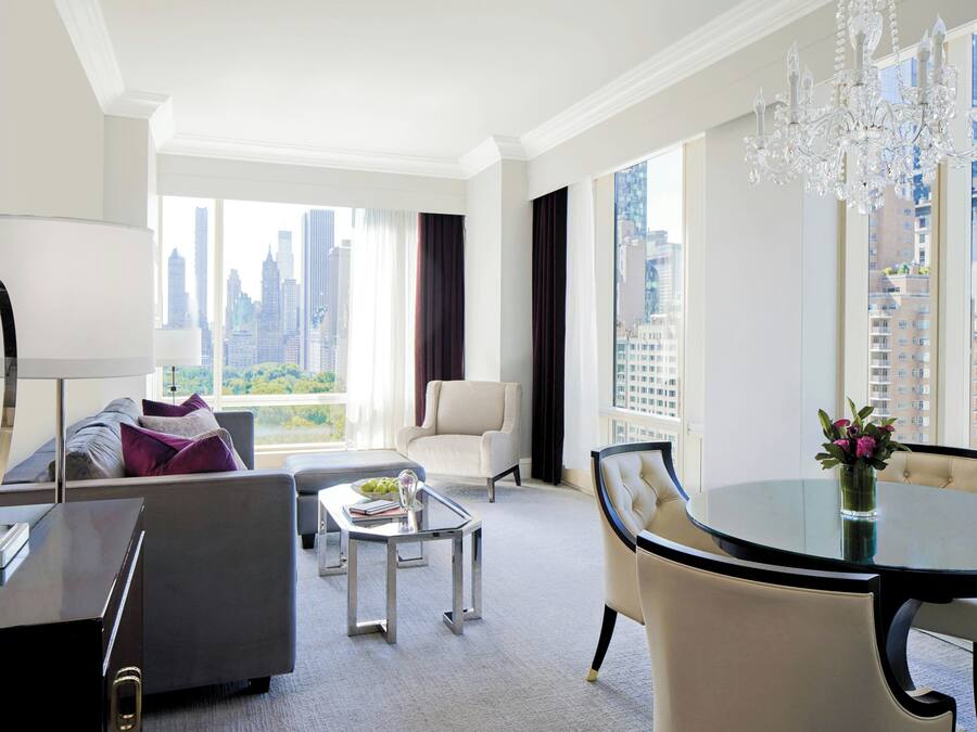 Una habitación de hotel moderna con vista a la ciudad, un área de comedor y una lámpara de araña grande.