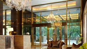 Un hall d’entrée luxueux, agrémenté d’un imposant lustre, de canapés en cuir, d’un comptoir d’accueil en marbre et de grandes fenêtres offrant une vue sur la verdure.