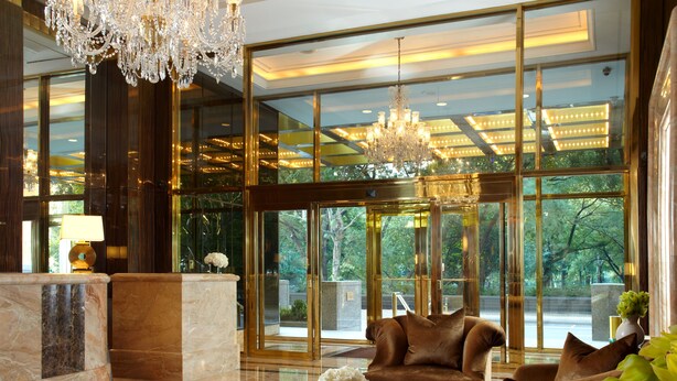 Een luxueuze lobby met een statig kroonluchter, leren banken, een marmeren receptiebalie en grote ramen met uitzicht op groen.