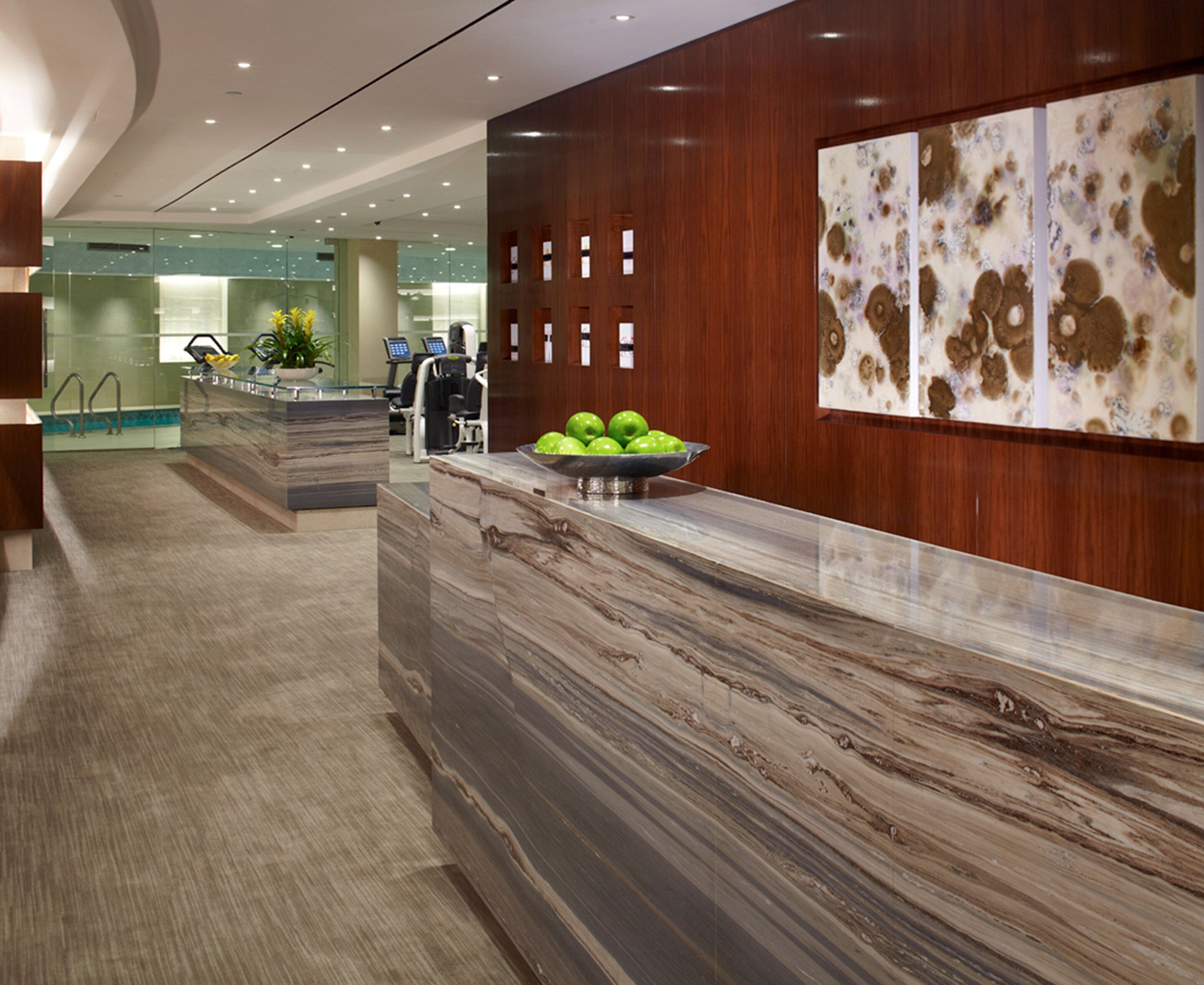 A modern reception area with a marble reception desk, a bowl of green apples, and a wall with abstract art.