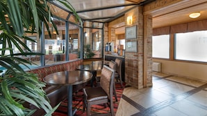Un restaurant aux murs de briques, doté de grandes fenêtres et proposant différents types de sièges, notamment des banquettes et des tables.