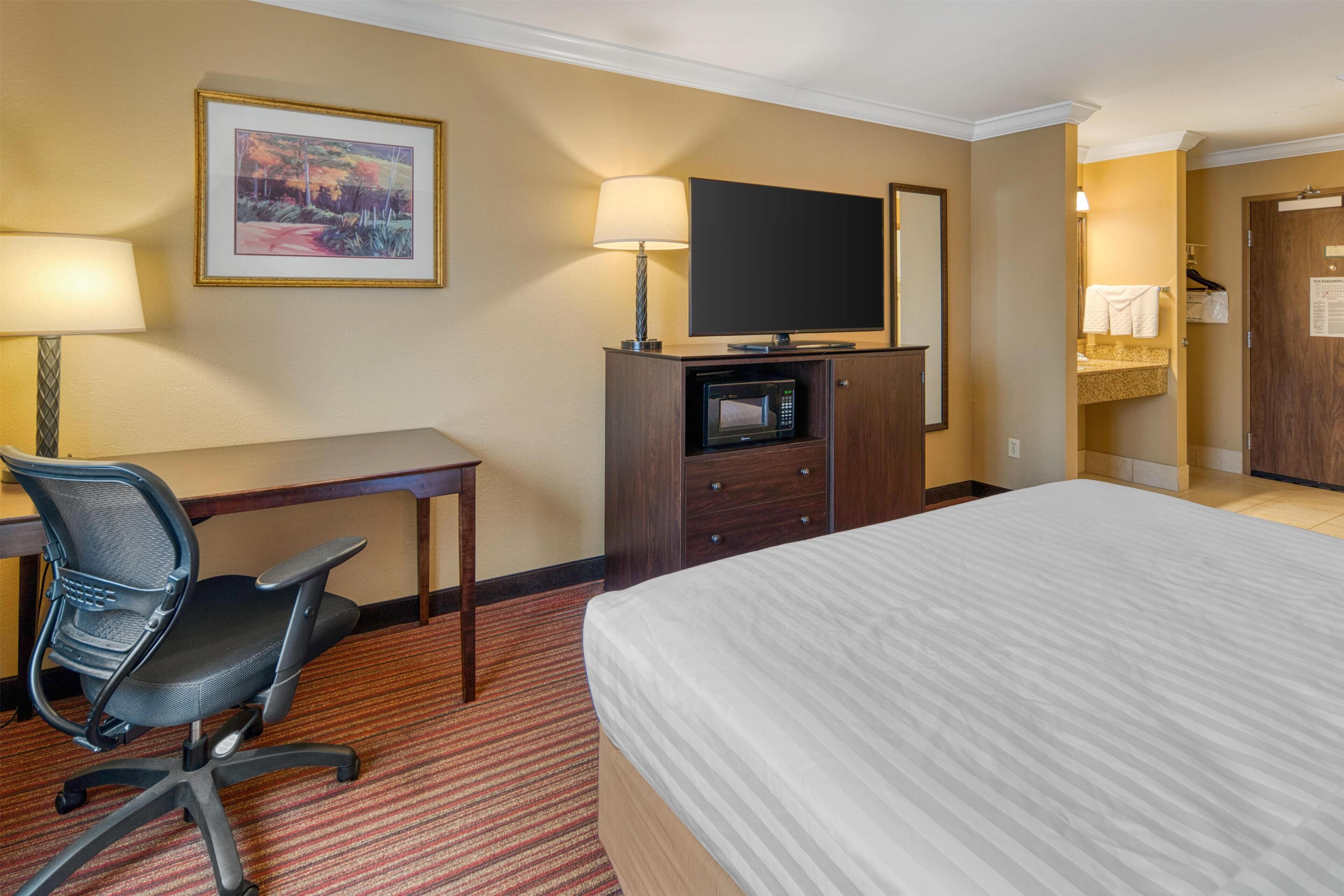 Hotelkamer met een bed, bureau, bureaustoel, televisie, magnetron en een badkamer met handdoekhouder.