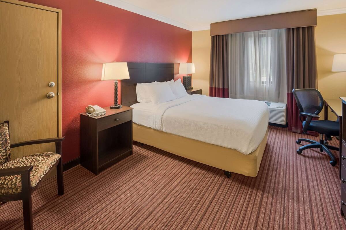 A hotel room with a bed, bedside tables, a chair, a desk, and a window with curtains.