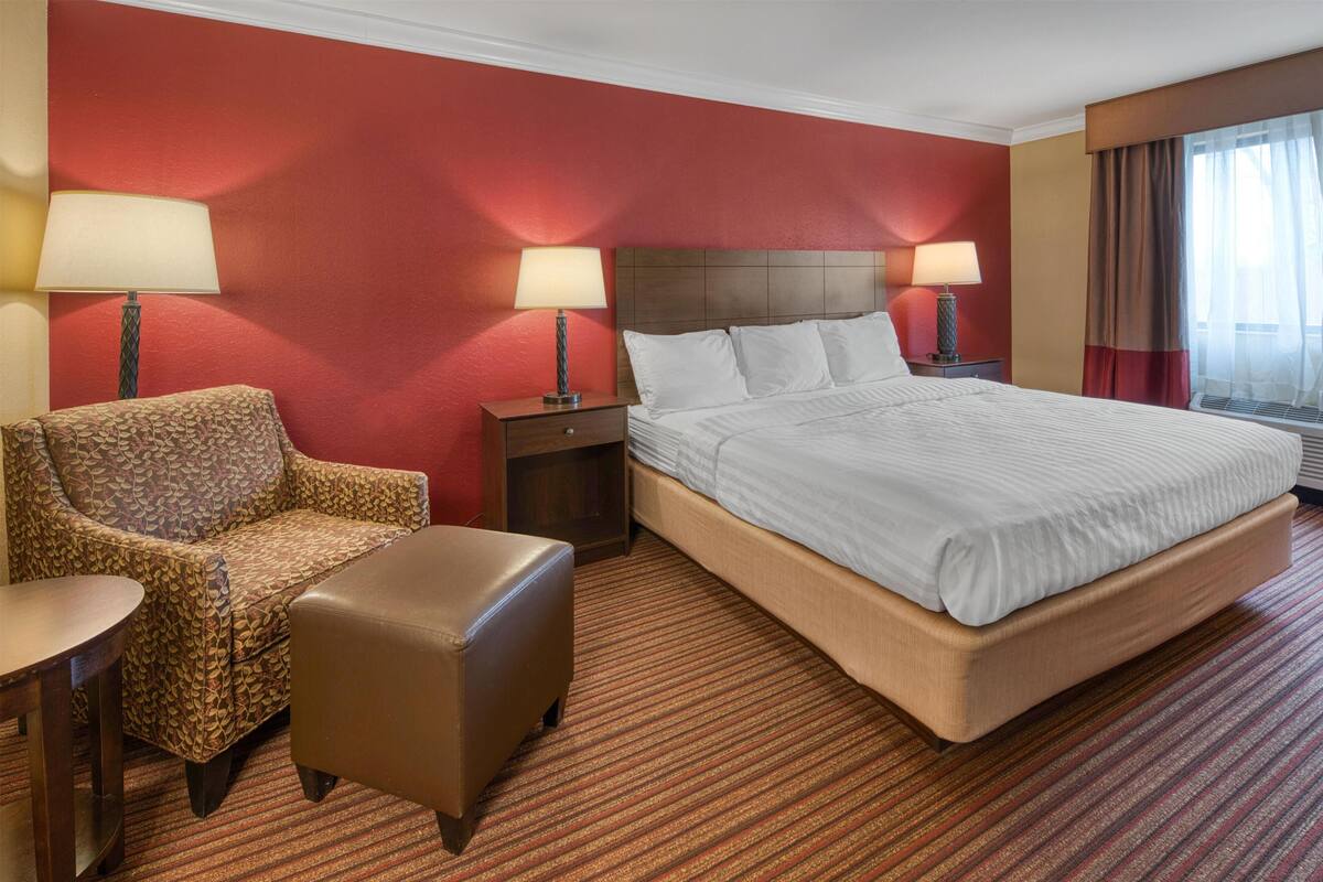 A hotel room with a bed, a chair, a small table, a nightstand, and two lamps.