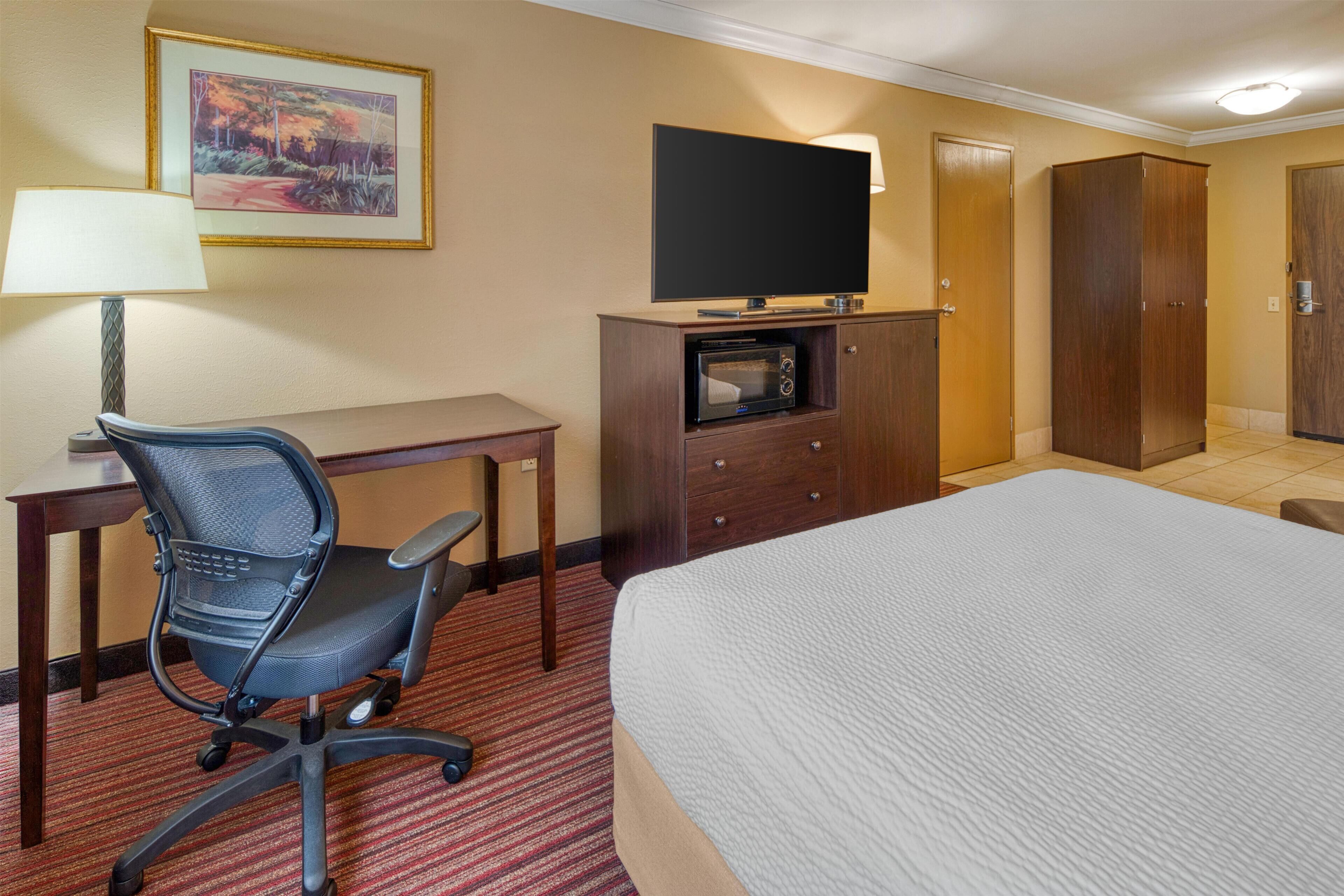 A hotel room with a bed, a desk with a chair, a television, a microwave, and a wardrobe.
