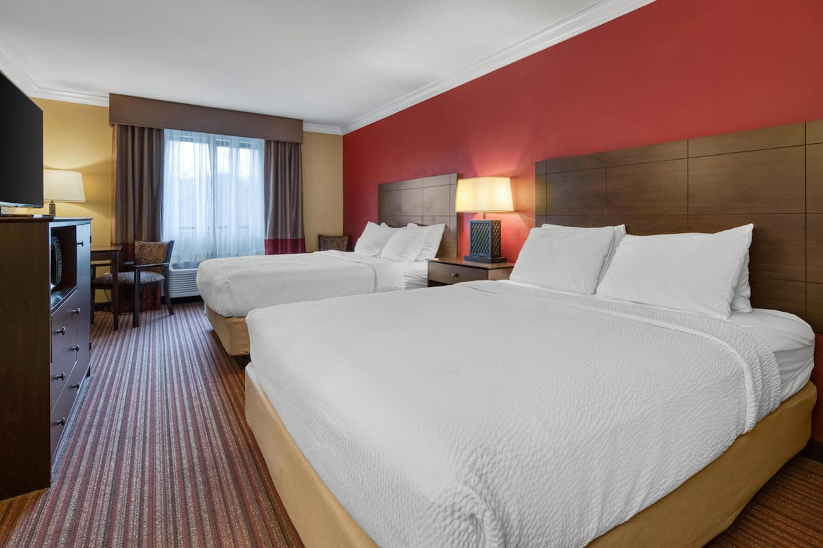 A hotel room with two beds, a desk, a chair, a TV, and a window with curtains.