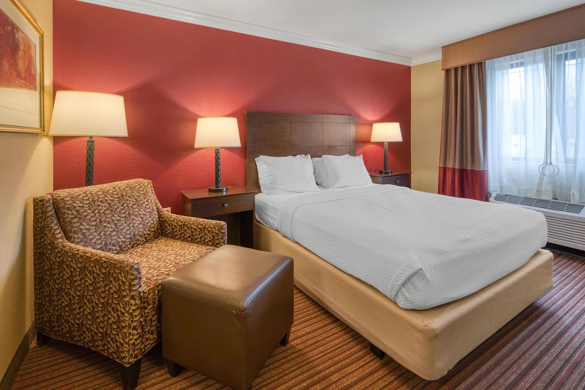 A hotel room with a large bed, a chair, a nightstand, and a window with curtains.