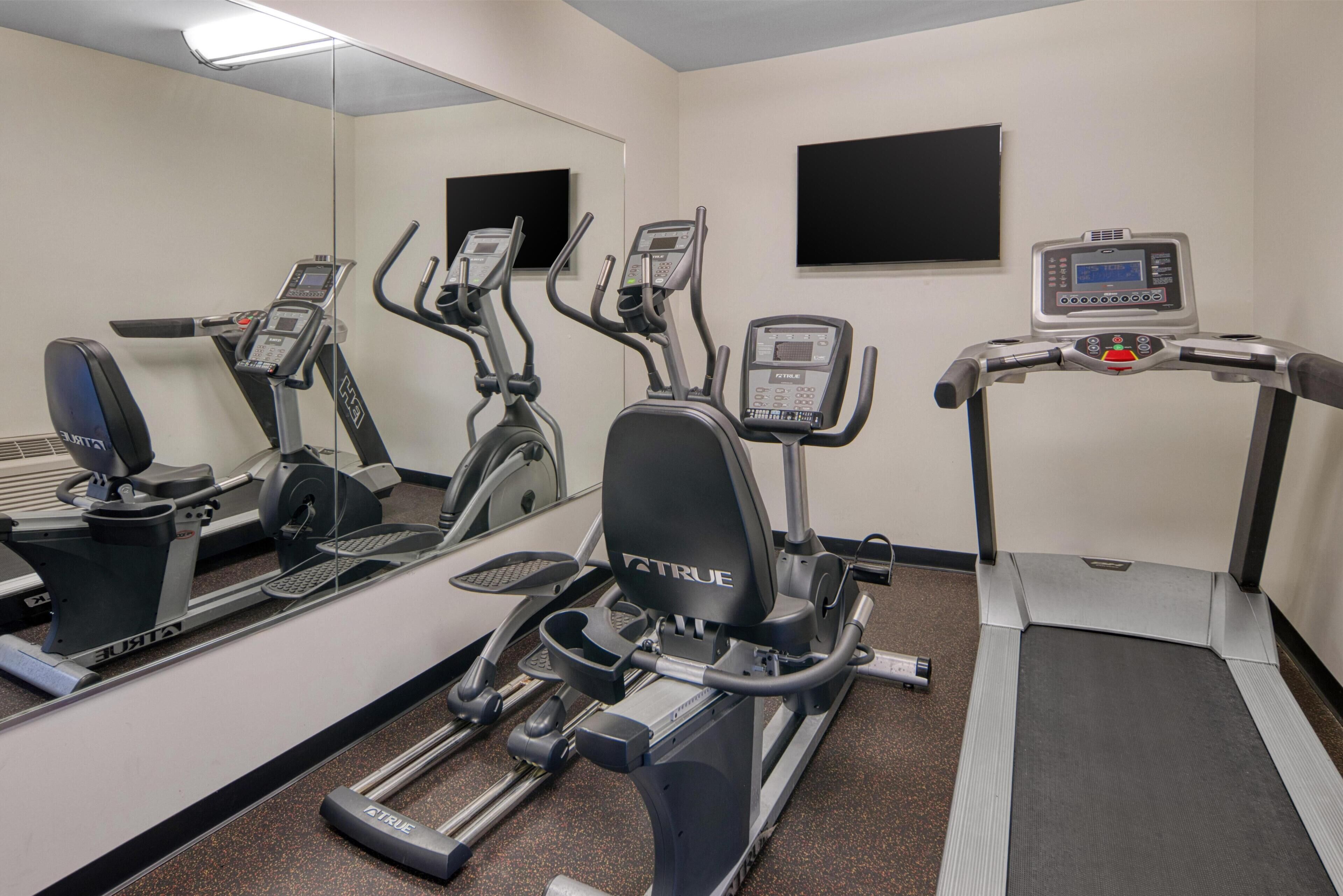 A gym with stationary bikes, a treadmill, and a mirrored wall.