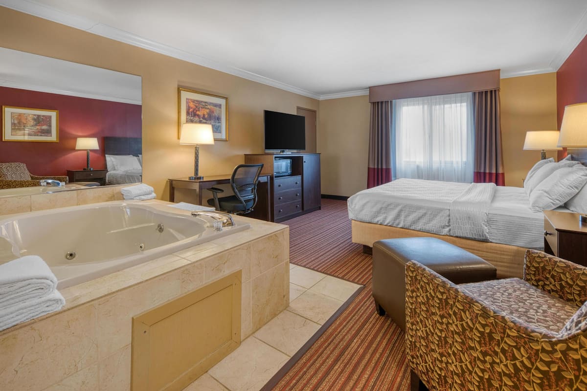 A hotel room with a large bathtub, a bed, a desk with a computer, and a television.