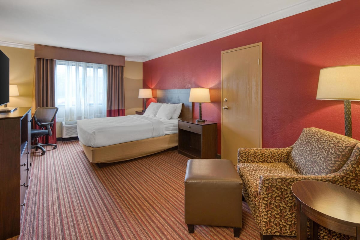A hotel room with a bed, desk, chair, ottoman, and a sofa.