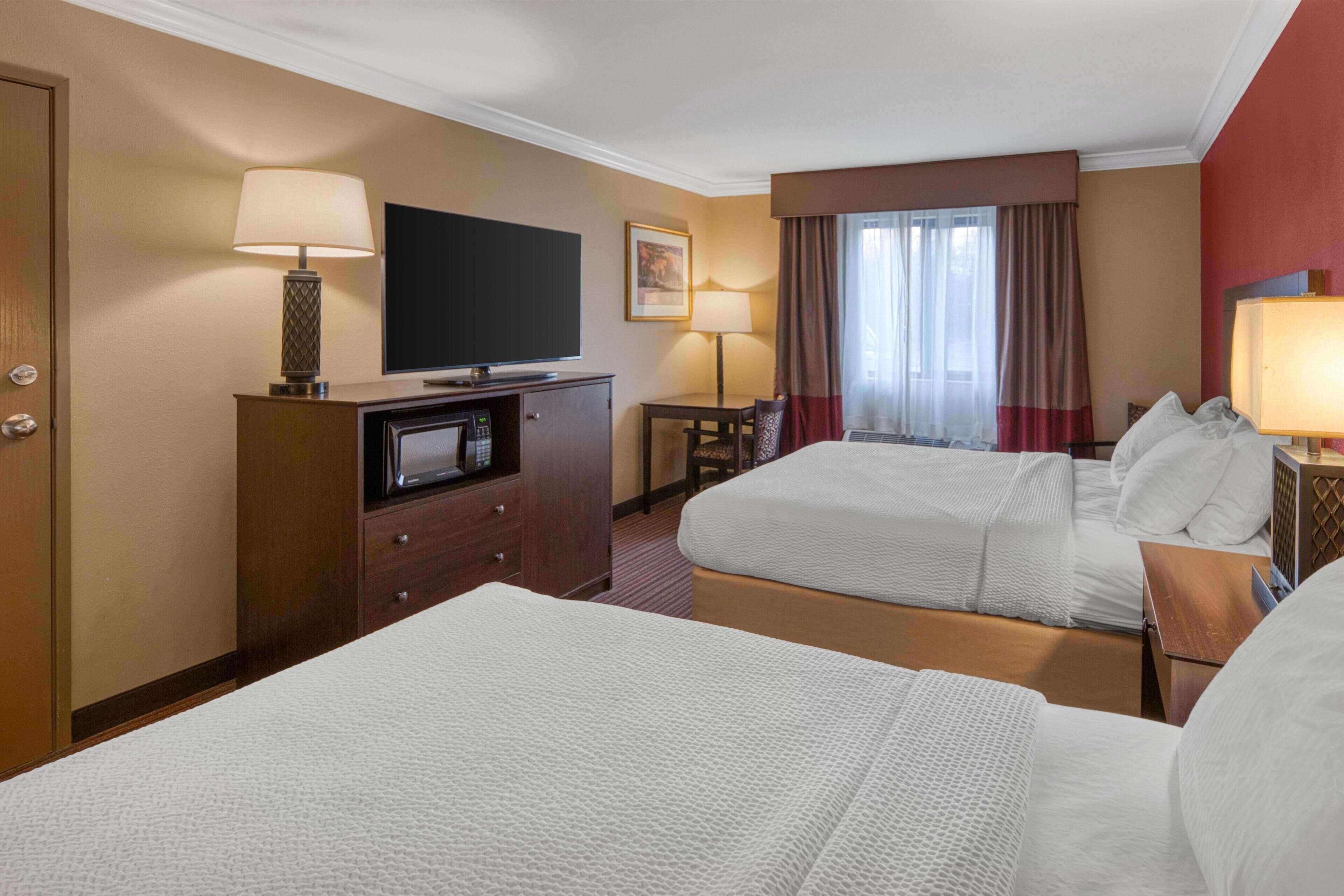 A hotel room with two beds, a TV, a desk, and a lamp.