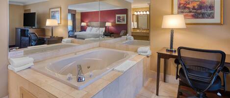 Habitación de hotel con una bañera grande, un escritorio con silla, televisión y espejo.