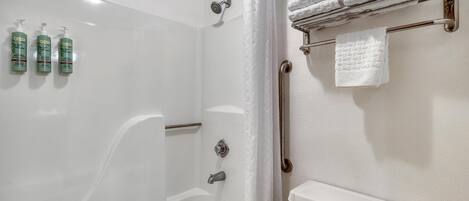 A bathroom with a bathtub, shower, and handrails. There are three bottles of shampoo on the wall.