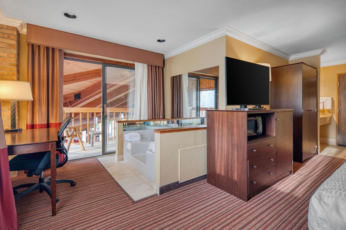 A hotel room with a desk, chair, television, wardrobe, and a view of the balcony.