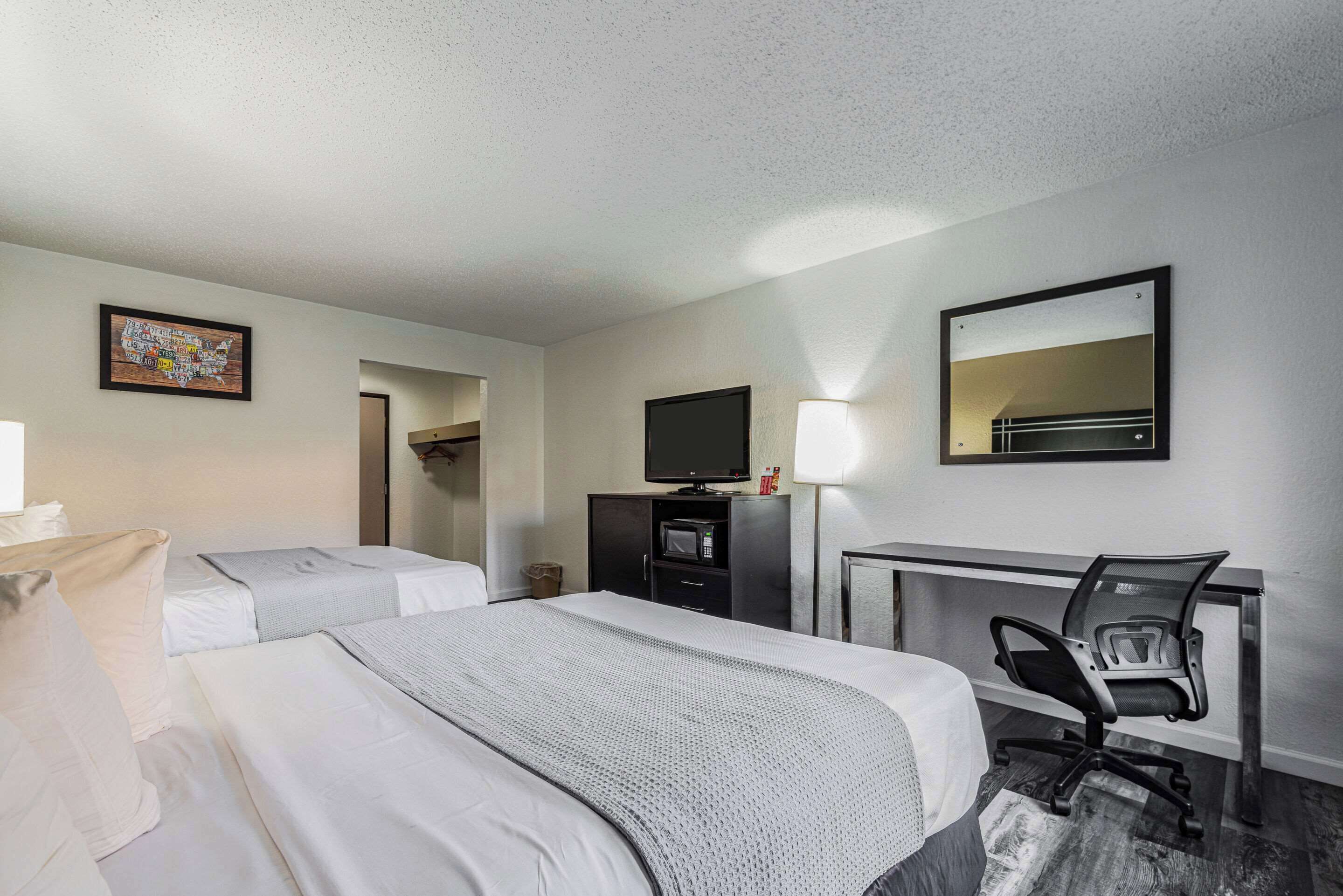 A hotel room with two beds, a desk with a chair, a television, a lamp, and a framed picture on the wall.