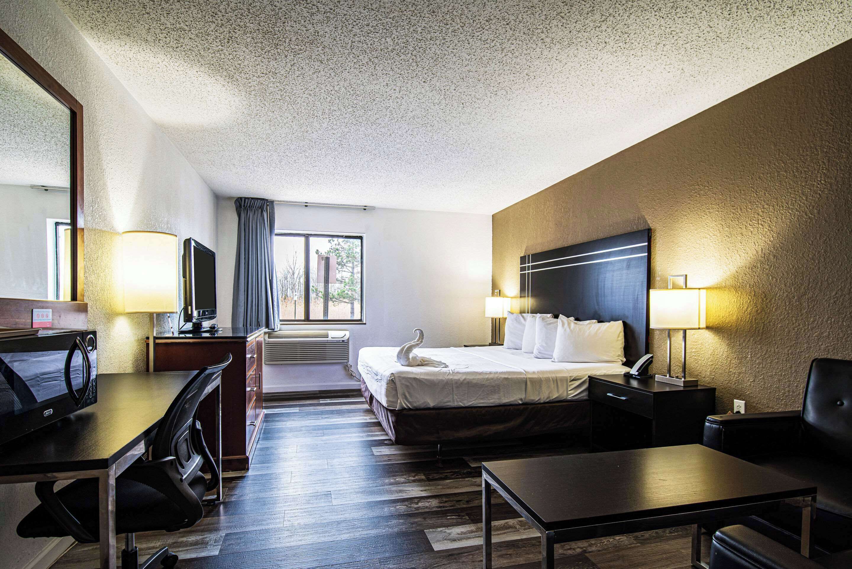 A hotel room with a bed, desk, chair, and a television.
