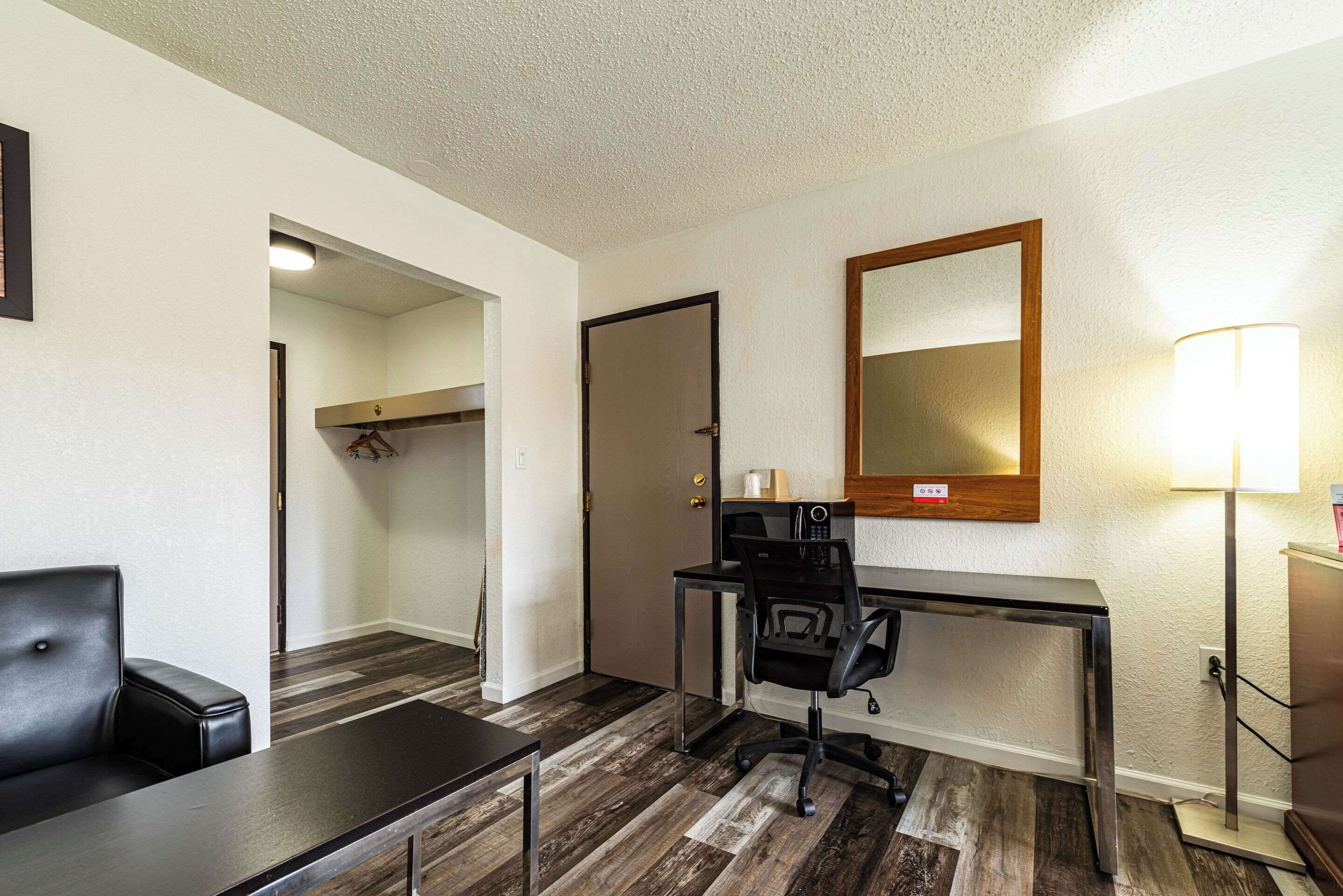 A hotel room with a desk, a black office chair, a coat rack, and a mirror on the wall.