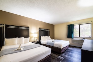 A hotel room with two beds, a nightstand, a lamp, a window with curtains, and a radiator.